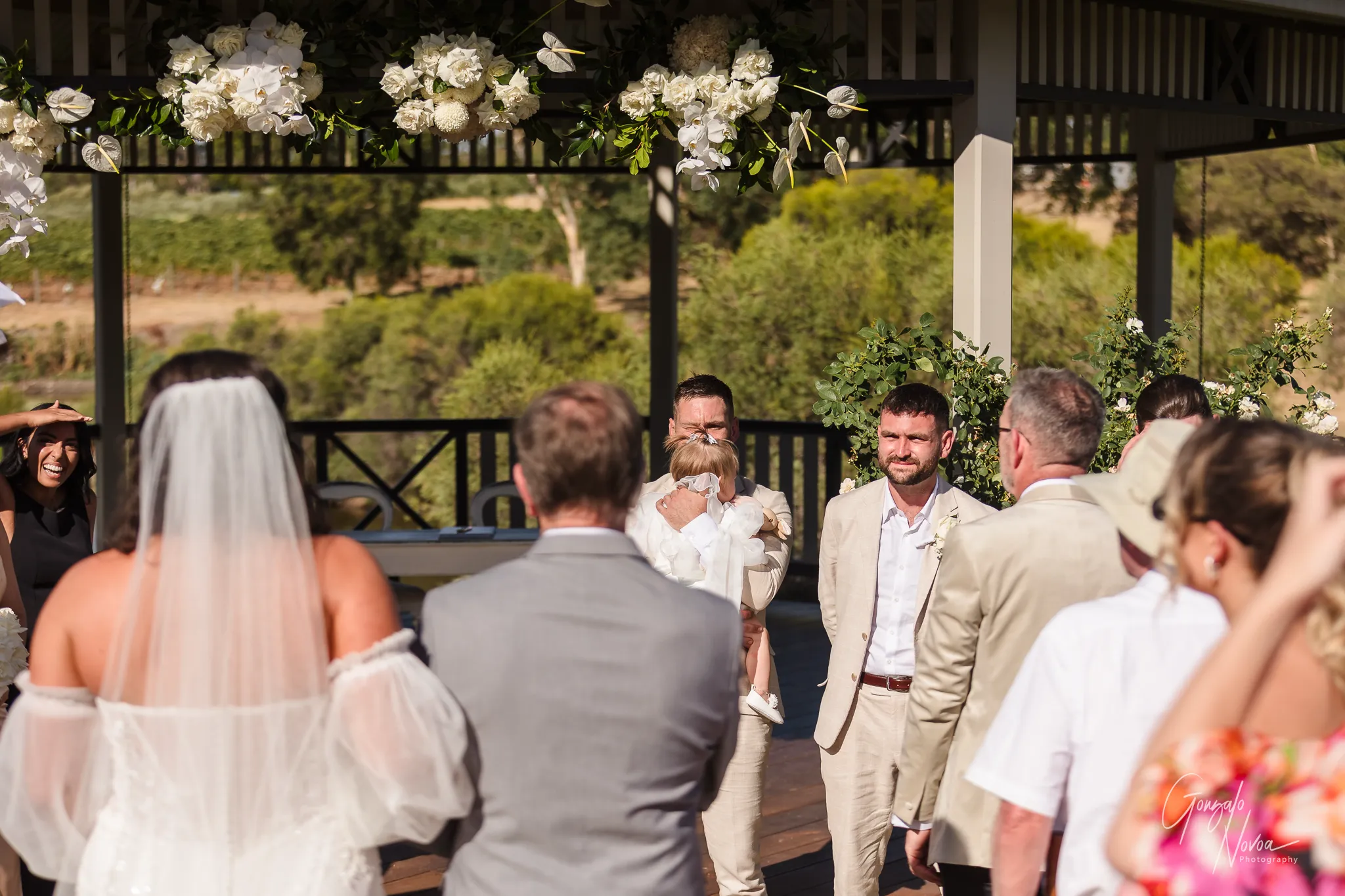Tahnee walks arm-in-arm with her father down the aisle at Sittella Winery, while groom James, holding their daughter Arlea, looks on with emotion as the bridal party and guests watch the beautiful moment unfold.
