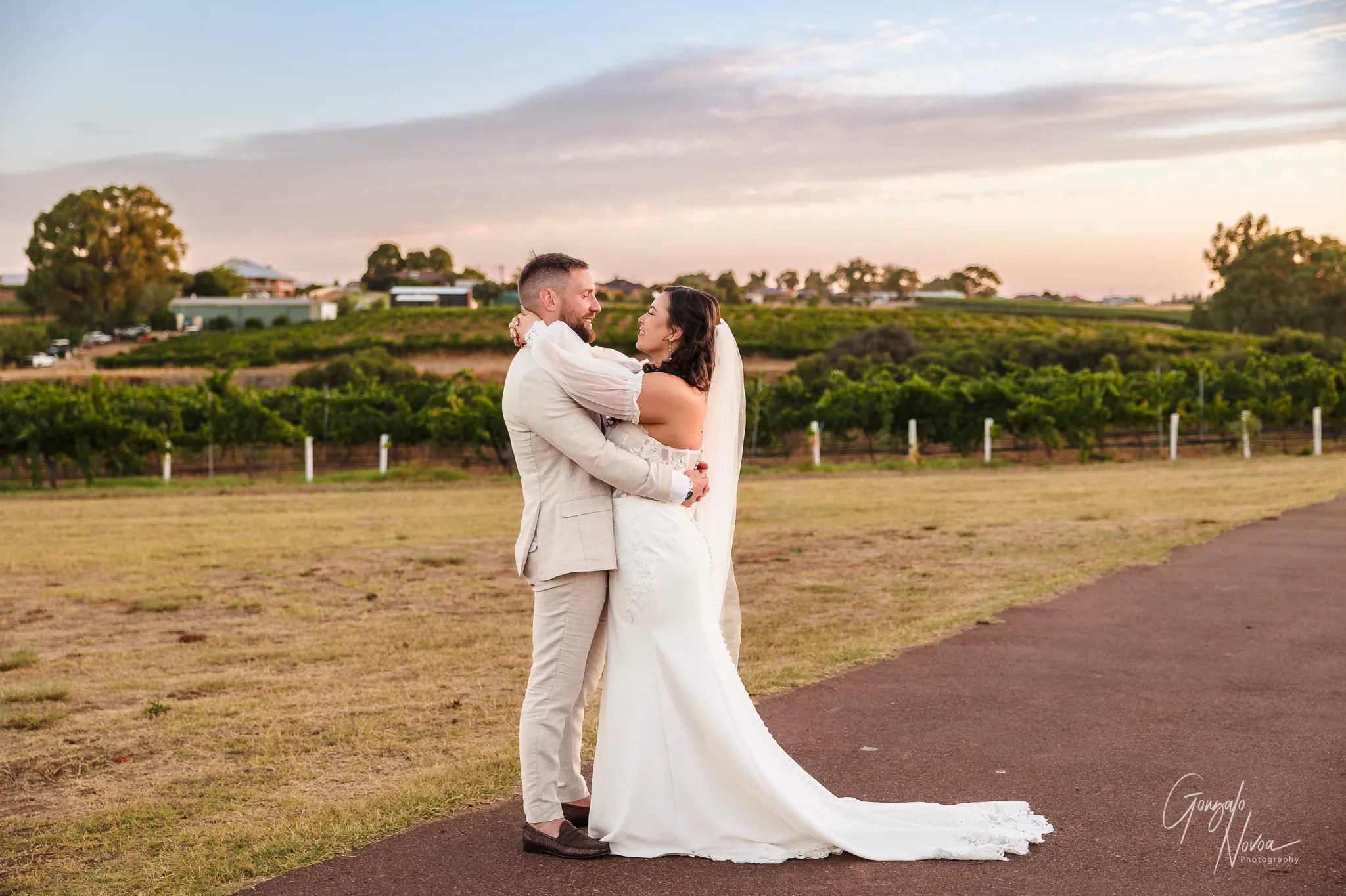 Bride and groom holding each other and smiling at sunset in the vineyard