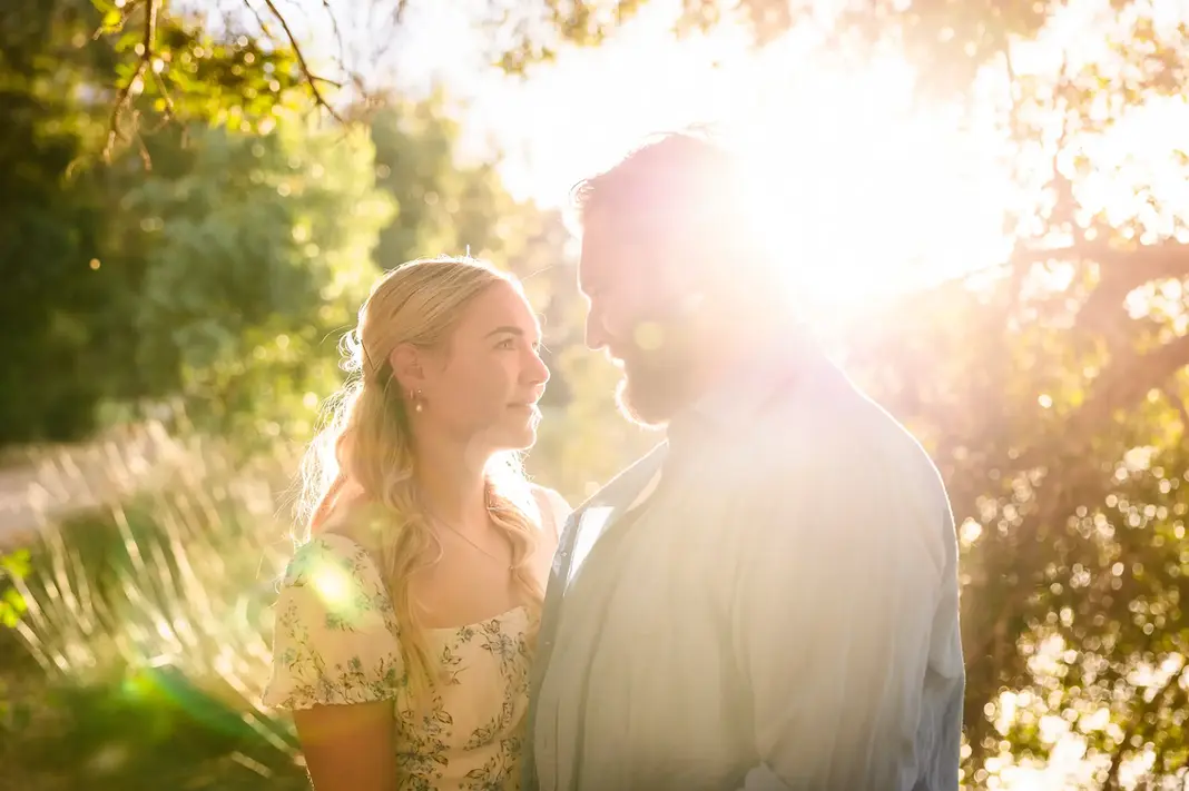 Colour photo of Faith and Alex gazing at each other with sunset light and trees in the background during their engagement shoot.