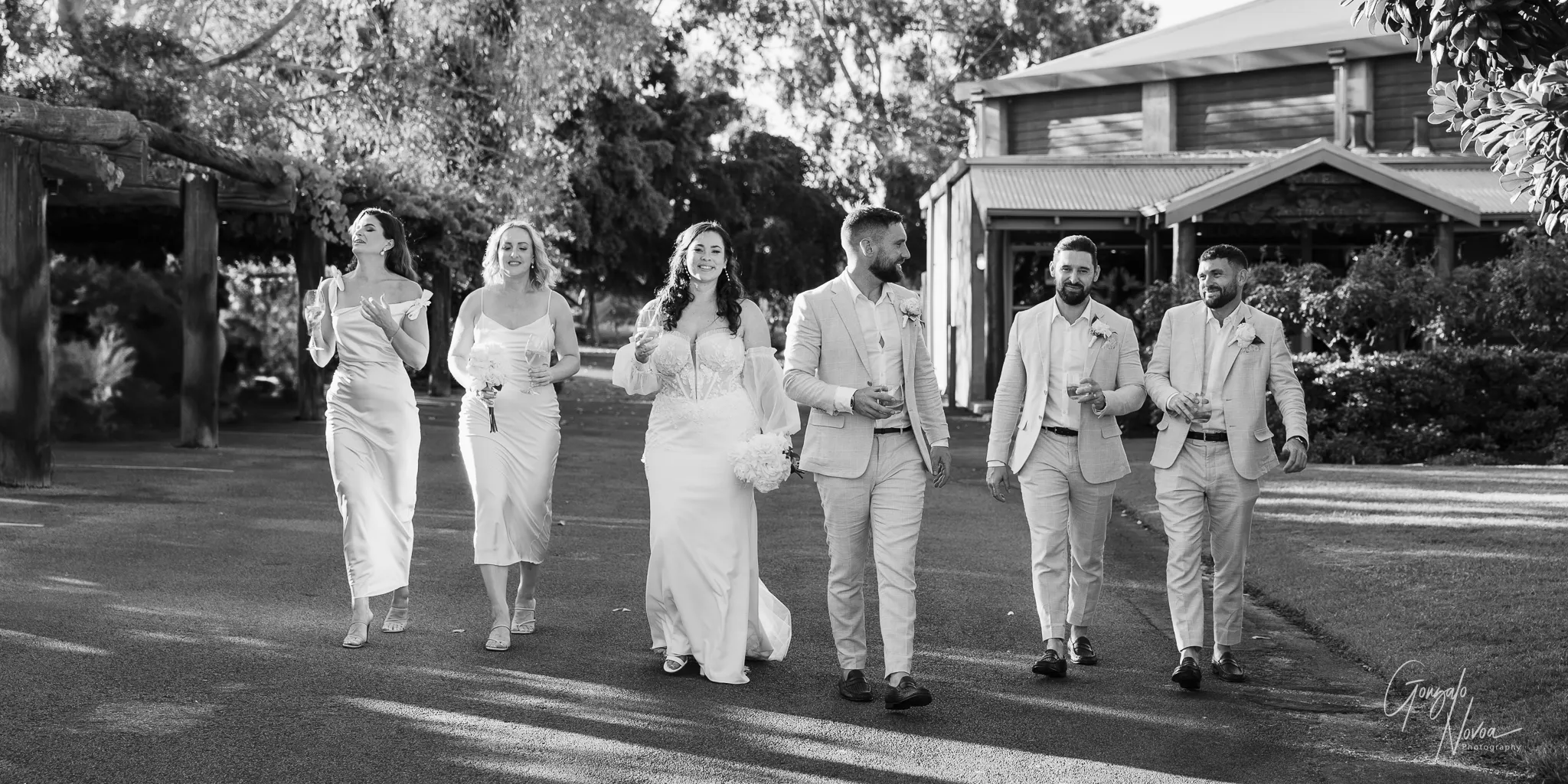 Tahnee, James, and their bridal party walking together at Sittella, holding drinks and smiling under the afternoon sun