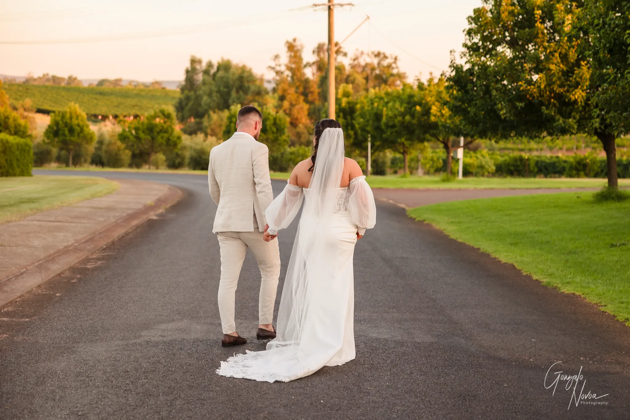 Bride and groom holding hands and walking down a country road at sunset