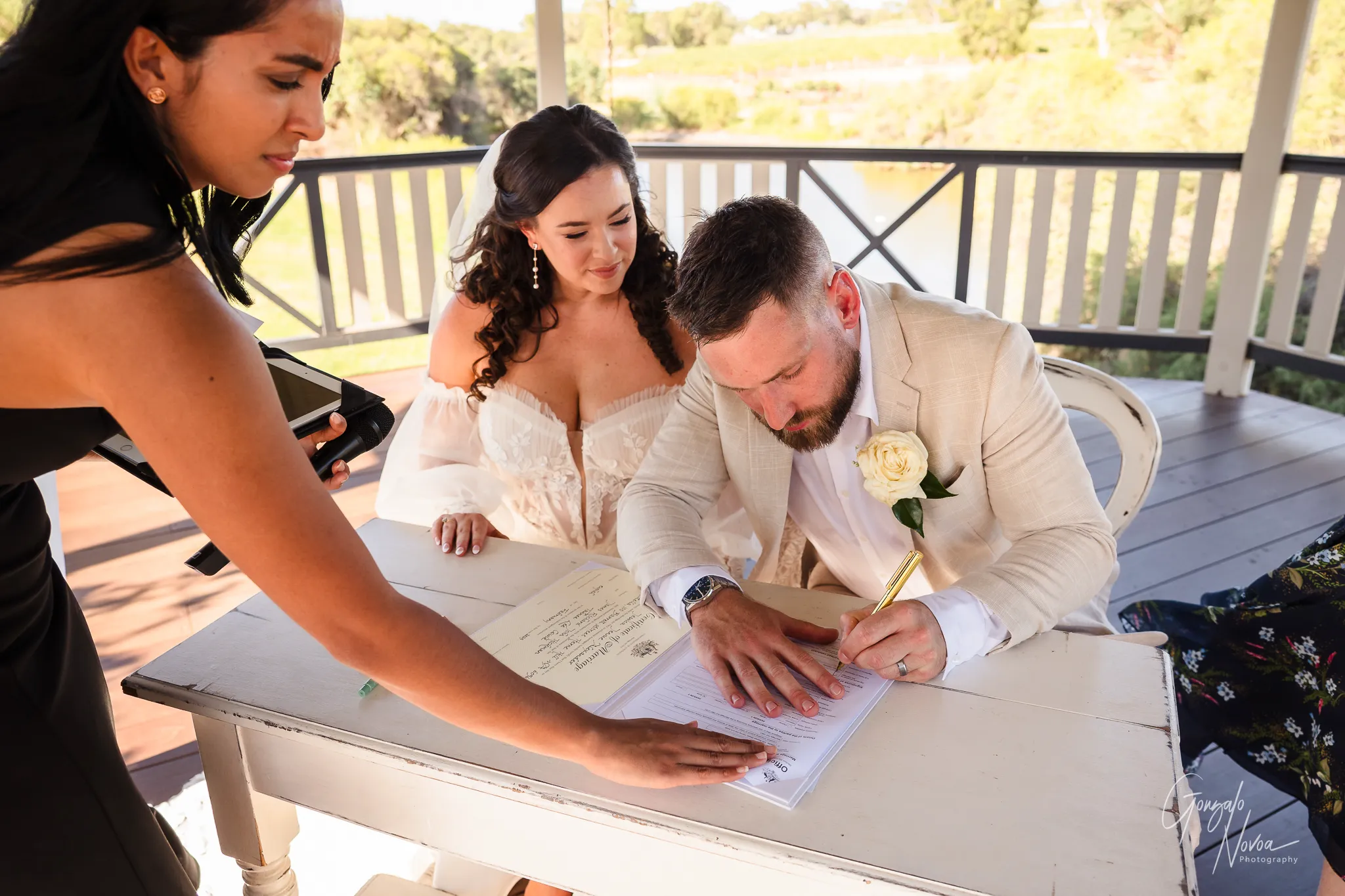 The groom signs the marriage certificate at Sittella Winery, with the bride sitting beside him smiling warmly and the celebrant assisting with the paperwork.