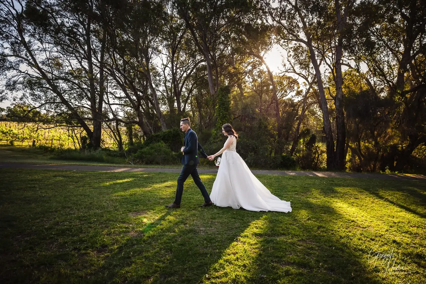 Bride and groom walking hand in hand through sunlit grounds at Oscar’s in the Valley in Herne Hill, WA.