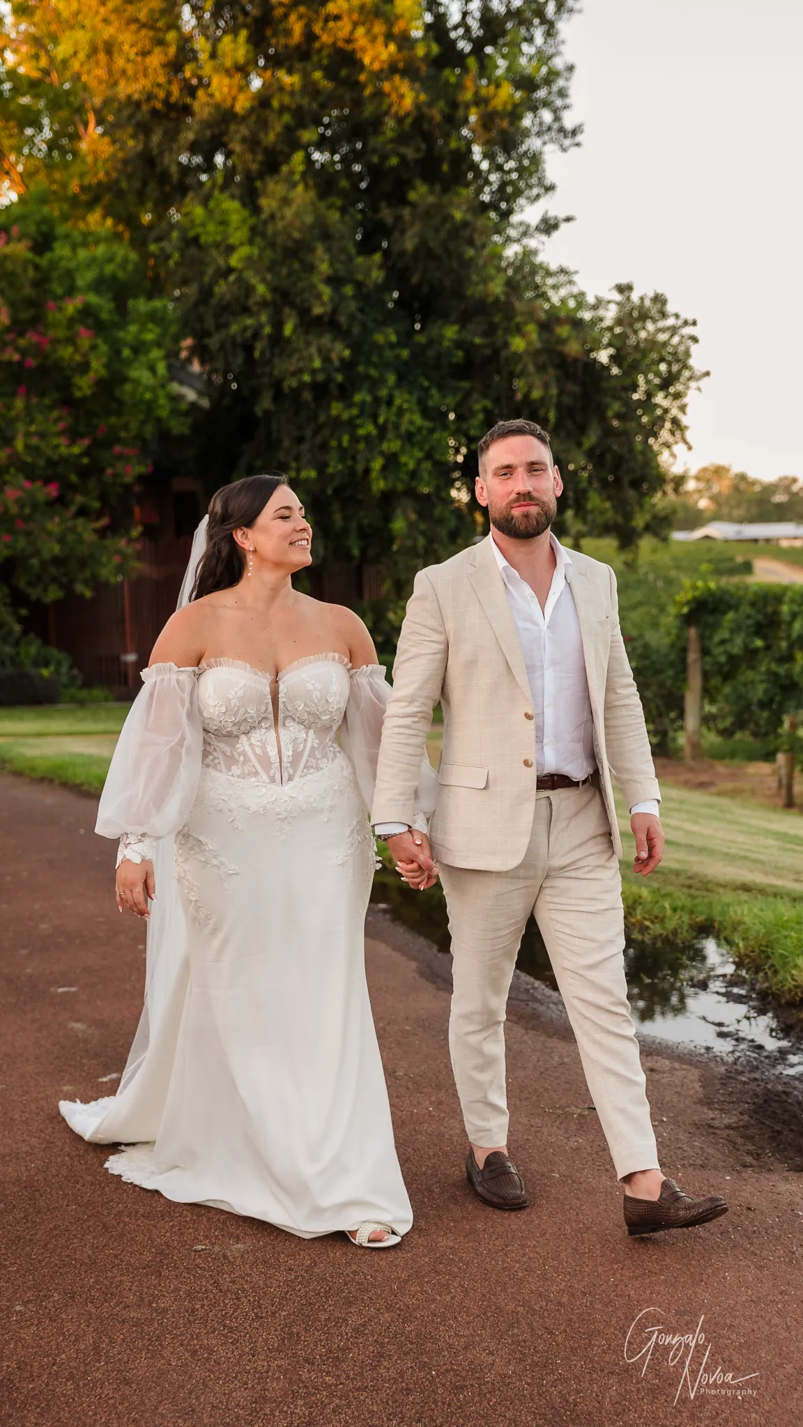 Bride and groom holding hands and walking along a path at sunset