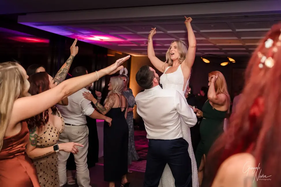 Bride being lifted by the groom on the dance floor at The Ritz-Carlton, Perth, with guests cheering and dancing around them.