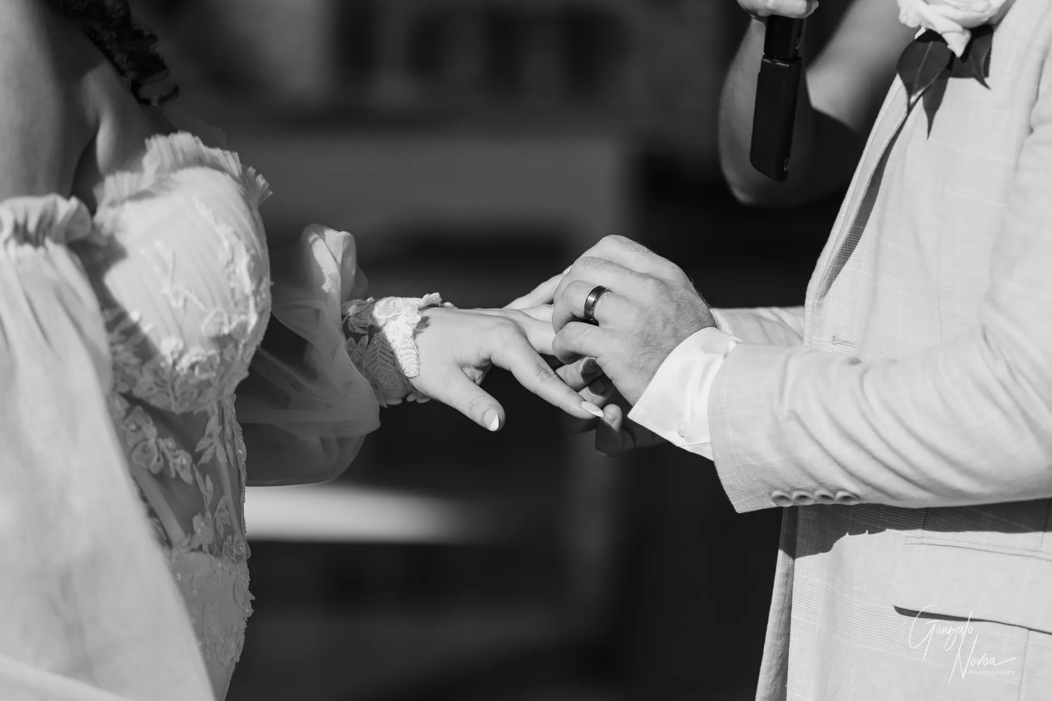 Close-up black-and-white photo capturing the bride placing the wedding ring on the groom’s hand during the ceremony at Sittella Winery, with soft tulle sleeves and delicate lace details visible.