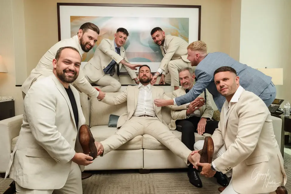 Groom sitting on couch while groomsmen and father playfully fuss over him during prep at Crown Towers Perth.
