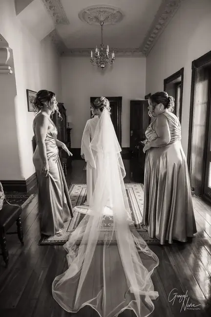 Bride with long veil standing in a hallway at Buckland Estate, surrounded by bridesmaids in satin dresses during wedding prep.