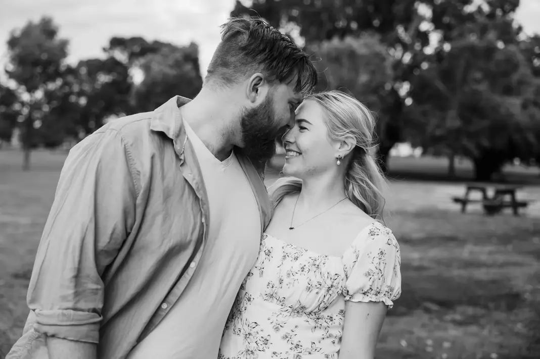 Black and white image of Faith and Alex smiling with their foreheads together in a park during their engagement session.