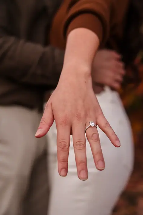 Close-up of Sandra’s extended hand showing her engagement ring, while Luis holds her from behind after their surprise proposal.