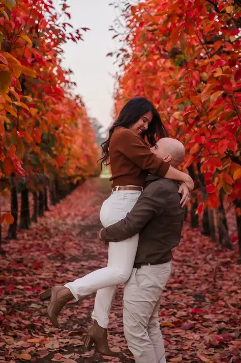 Luis lifts Sandra in a joyful embrace along a vibrant autumn orchard path, with her legs curled back and both of them smiling at each other.