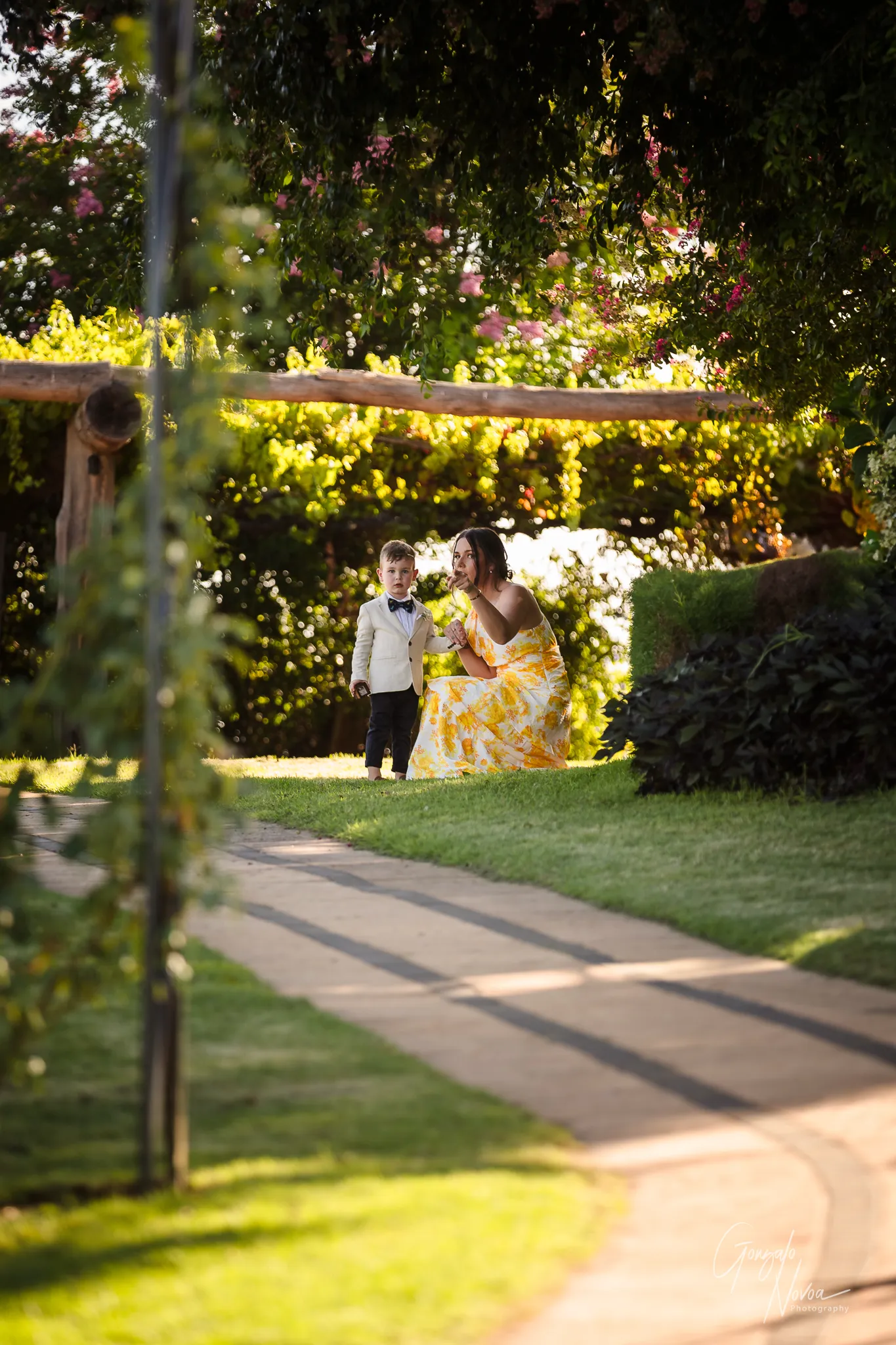 The ring bearer, dressed in a cream jacket and bow tie, stands with a woman giving encouragement before walking down the aisle at Sittella Winery.