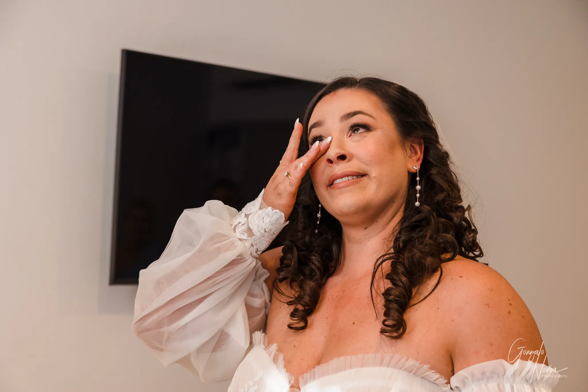 Bride Tahnee wipes away tears of joy after an emotional first look with her father on her wedding day, wearing her off-the-shoulder gown and pearl drop earrings.