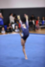 a female gymnast posing on the gymnastics floor with one leg up and both arms up