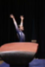 a female gymast in a blue leotard standing behind a vault with her arms straight up over her head in a finish pose