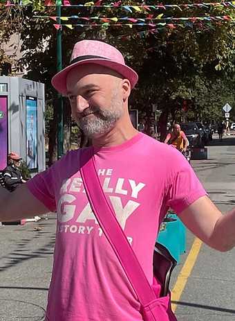 Glenn Tkach standing in a Vancouver street wearing a pink "Really Gay History" t-shirt and pink fedora