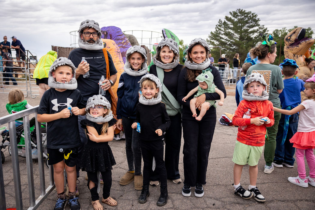 Group of adults and children in black and purple dinosaur-themed outfits posing together outdoors