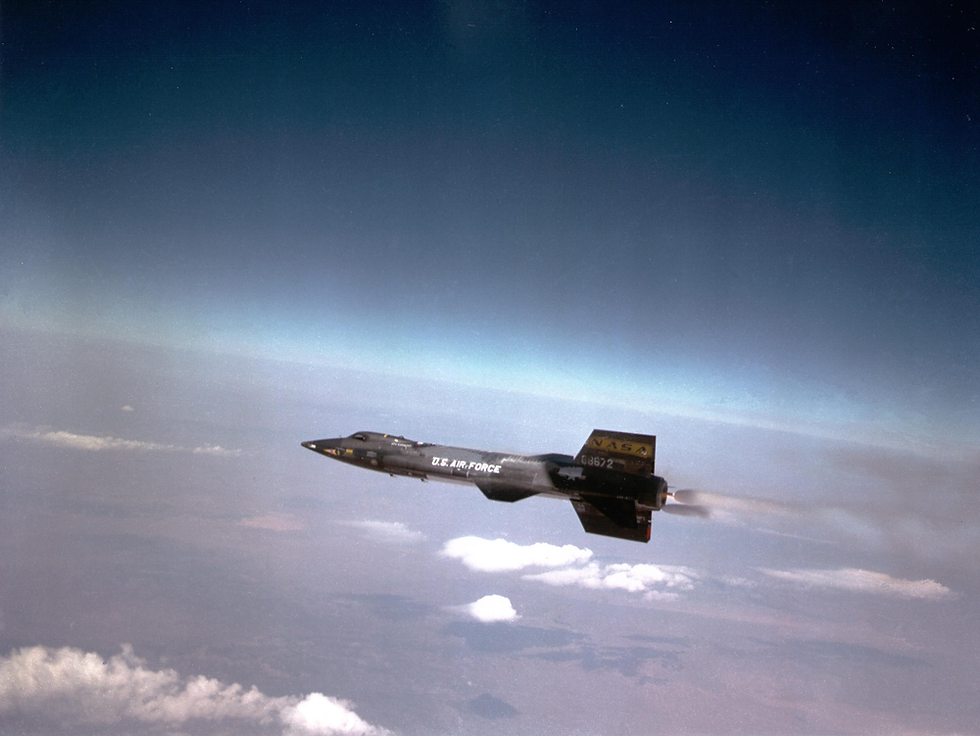 NASA / Air Force X15 aircraft flies over clouds with "U.S. Air Force" text. Blue sky, horizon, and smoky trail visible. Dynamic and high-altitude setting.