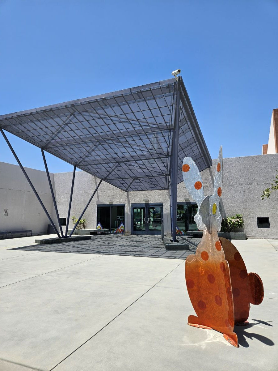 Animal rust-colored sculpture in the right foreground. In the background the entrance to the Children's Discovery Museum