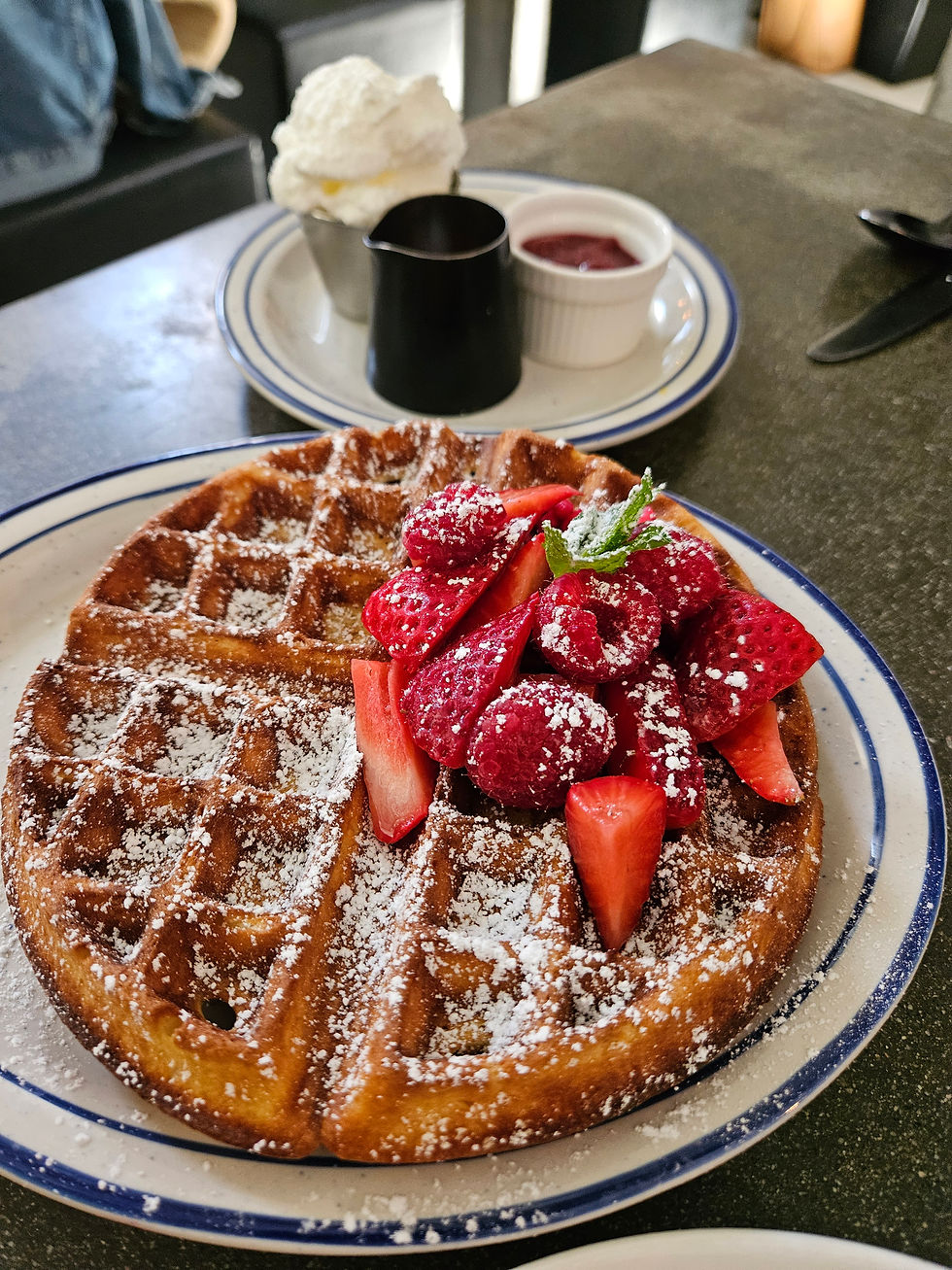 Waffle with strawberries next to a little pitcher of syrup.