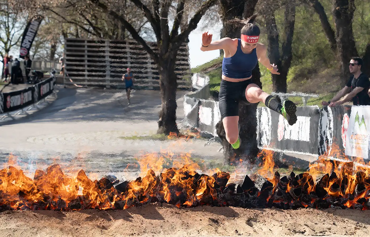 Female runner jump from fire obstacle at Spartan Race Munich