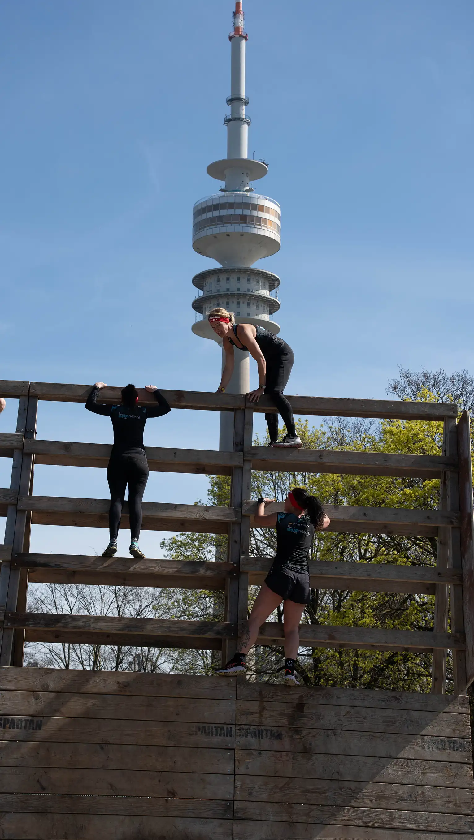 Female athlete climbs a tall wall during Spartan Race Munich, showing focus, power, and determination.