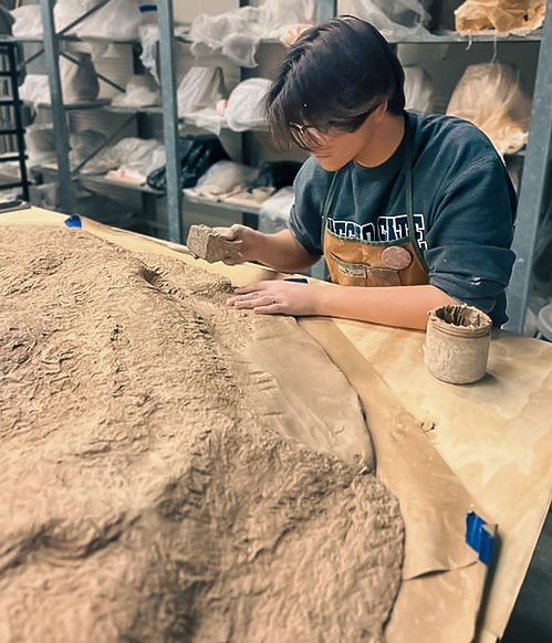 Miguel adding texture to his nearly 6FTx6FT sculpture "I hope you find what you're looking for." using a small brick.
