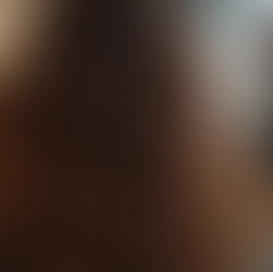 Długie, faliste włosy kobiety z przodu w salonie fryzjerskim; w tle rozmyci ludzie. Jasne oświetlenie, ciepła kolorystyka.