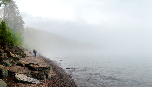 Two people walk along the shore of Lake Superior.