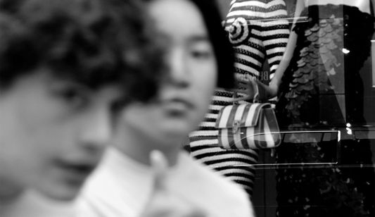 Two teenagers look at the camera and one gives a thumbs up in front of a storefront.