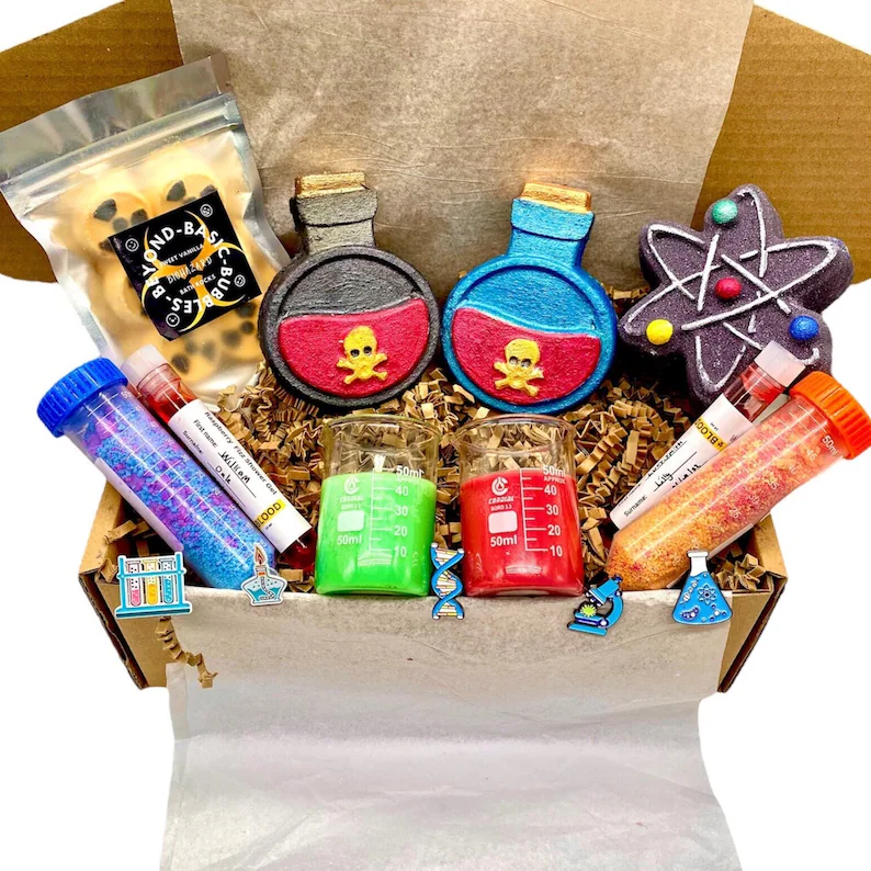 A cardboard box containing a series of bath bombs, bath salts and bubble bath shaped like different molecules, beakers and other scientific items
