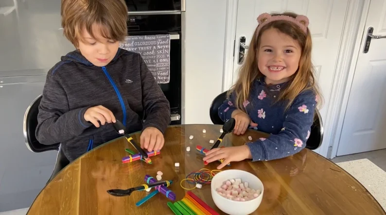 Two children using pencils, elastic bands and spoons to create marshmallow catapults