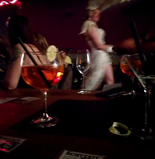 Stimmungsvoller Abend im Echtzeit Köln: Ein kühler Aperol Spritz im Vordergrund, während im Hintergrund eine Burlesque-Performance auf der Bühne für Begeisterung sorgt. Perfekte Kombination aus Drink und Show.