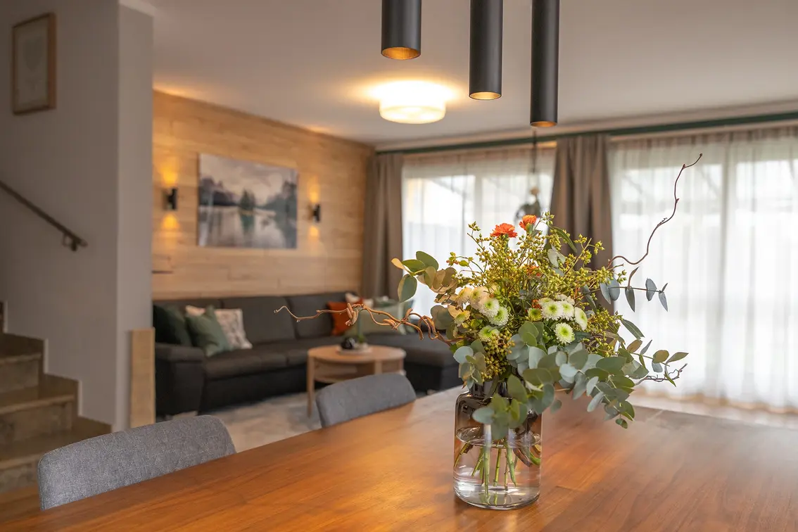 Dunkelgraues Ecksofa mit Holzwand, grauen Vorhängen und schwarzen Lampen