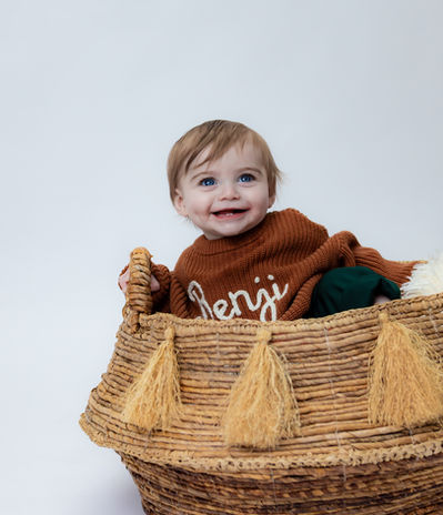 Smiling toddler sitting inside woven basket.