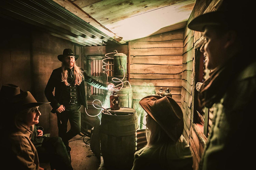 Cowboys in a rustic wooden shed around barrels and hoses, one man standing by a green tank, warm dim light, serious mood