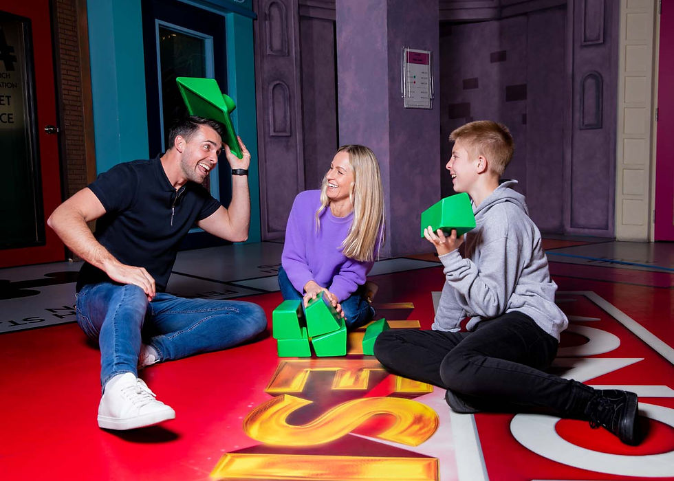 Smiling family sits on a colorful floor, stacking bright green blocks in a playful indoor game with a large 5 visible.
