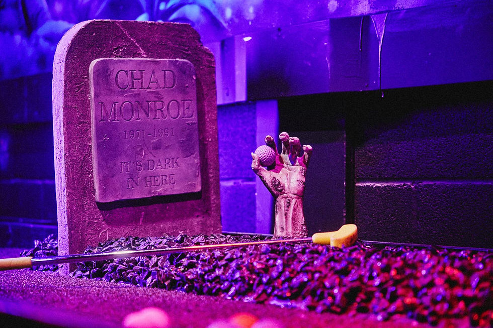 Spooky purple mini-golf scene with tombstone reading CHAD MONROE 1971-1991 IT'S DARK IN HERE and a zombie hand holding a golf ball.