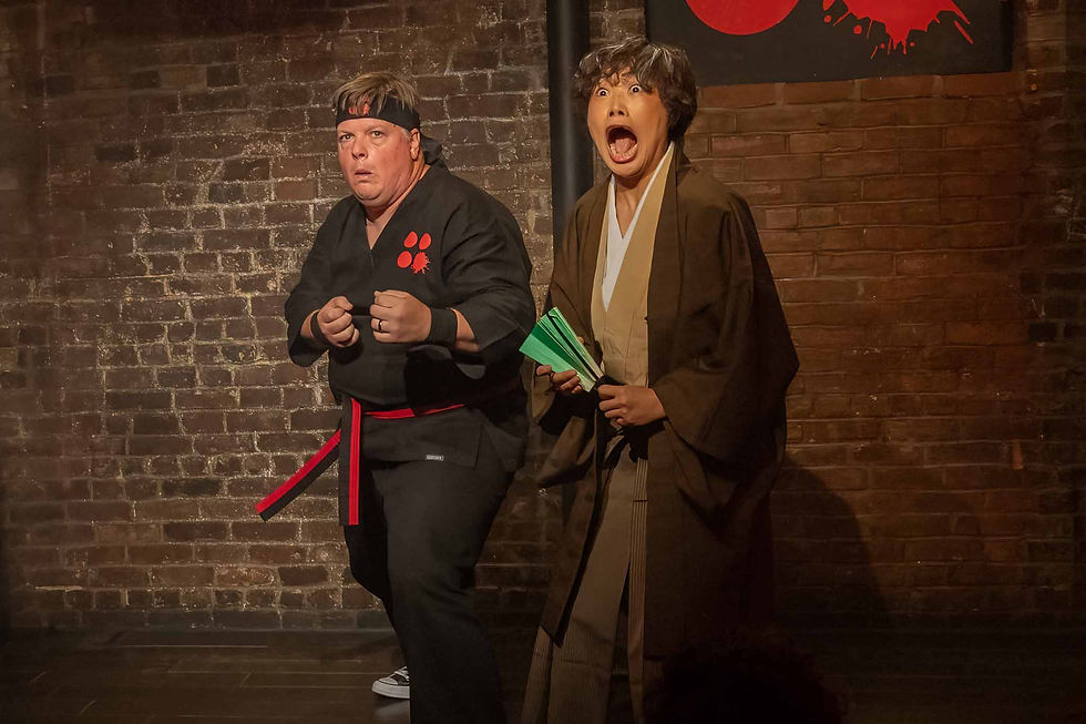 Two costumed performers on a brick stage, one in black ninja gear and one in brown robes shouting, with a red ninja symbol behind them.