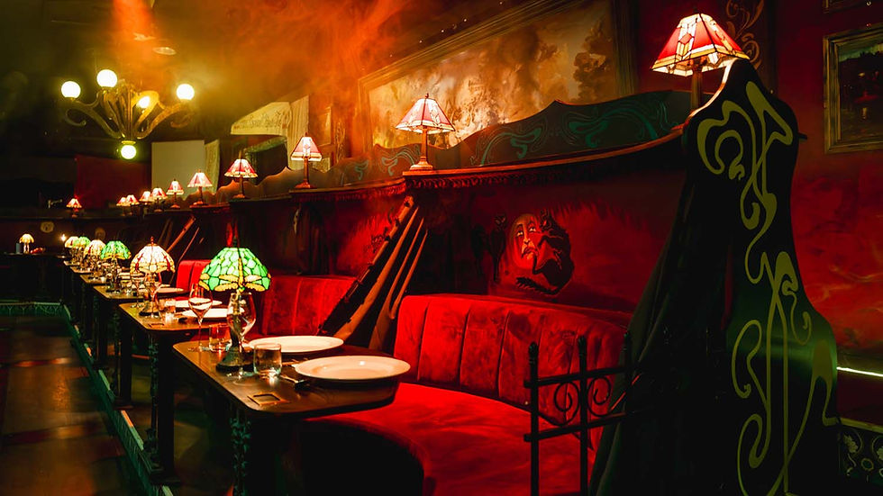 Dimly lit restaurant with red velvet booths, decorative lamps, and artsy murals. Plates and glasses set on dark wooden tables. Cozy ambiance.