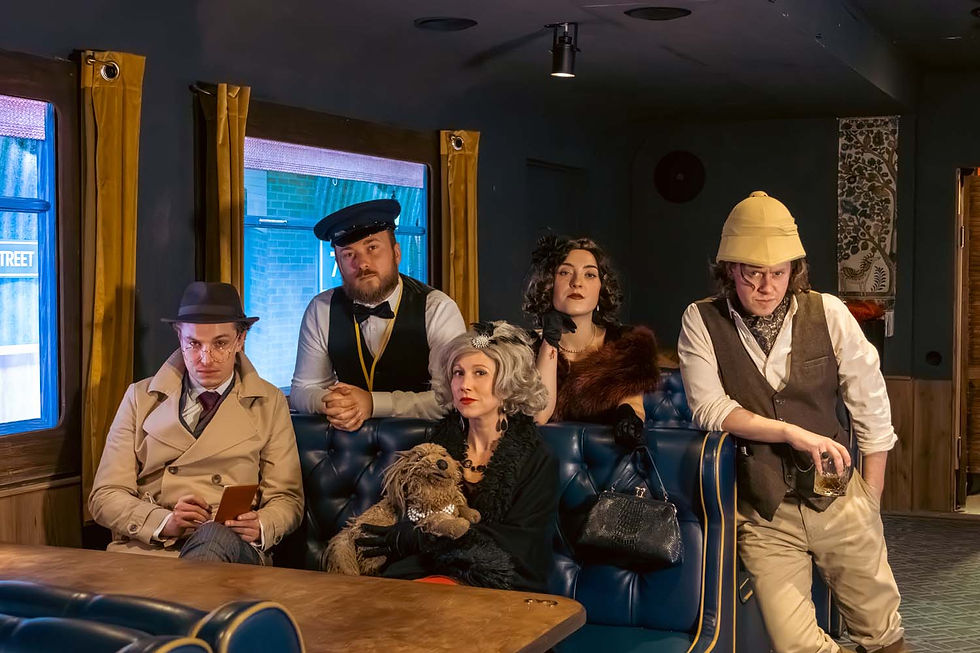 Five people in vintage detective-style outfits pose in a dim diner booth; one holds a drink, another a stuffed dog.