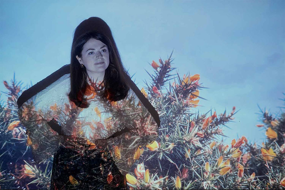 Woman standing against a blue sky and cactus projection, her dress and face overlaid with orange flowers, calm expression