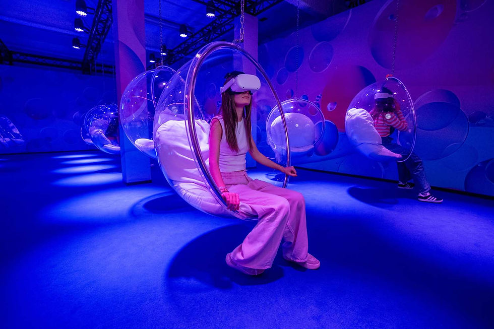 A person in VR goggles sits in a clear bubble chair in a futuristic, purple-lit room with playful bubble patterns, evoking a surreal feel.