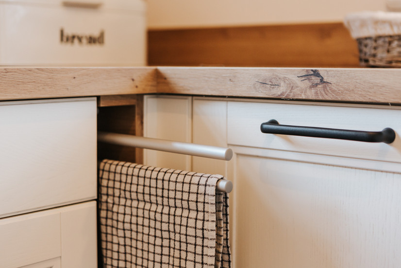 Detailansicht eines reduzierten Küchenunterschranks mit matter Front mit schwarzem Bügelgriff, ausziehbarer Handtuchstange aus Metall und Arbeitsplatte in Eiche natur.