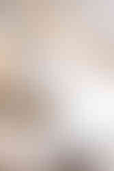 Detailansicht moderner Küche mit weißen Fronten, dunkler Stein-Arbeitsplatte und Spüle vor Fenster, im Vordergrund drei Glas-Pendelleuchten und Polsterstuhl am Essbereich