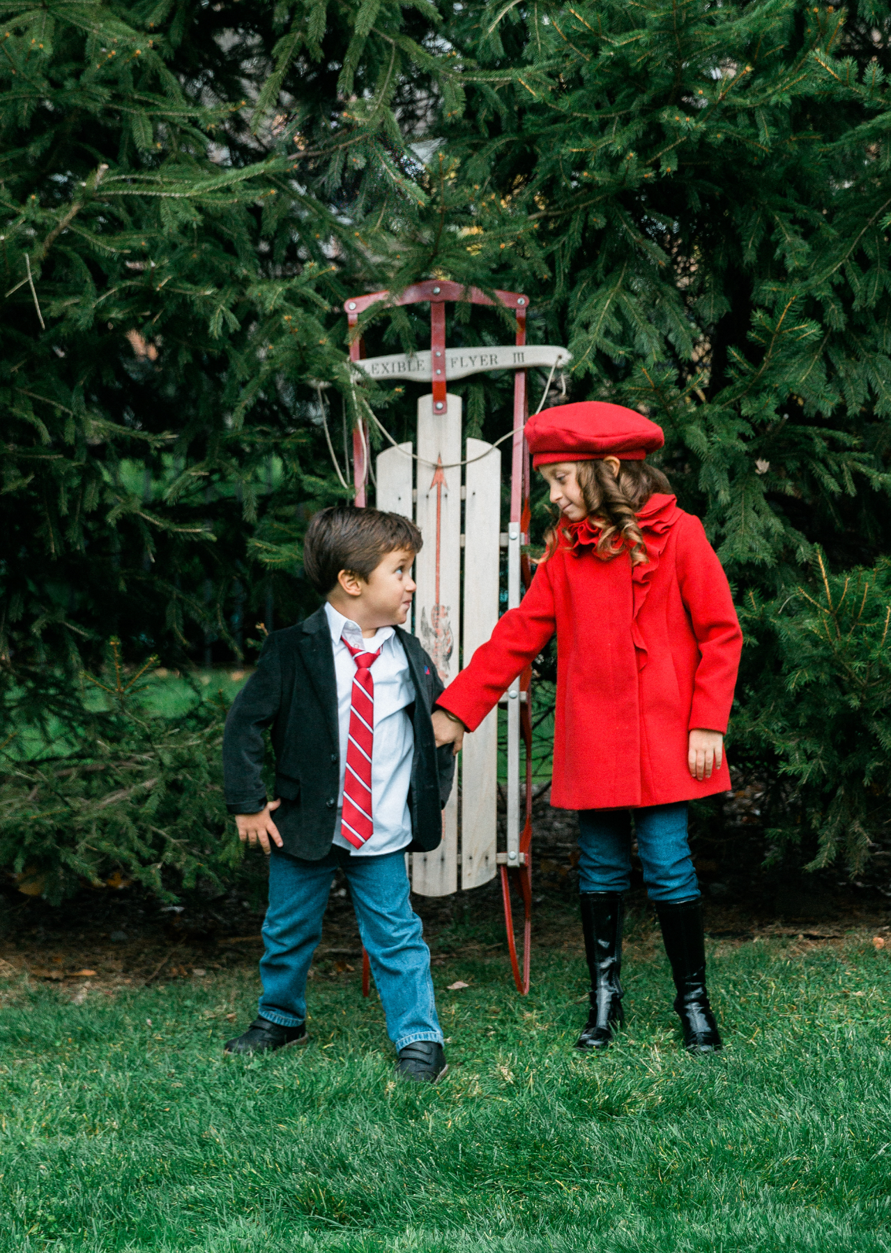 Two children standing beside a vintage sled at a tree farm.