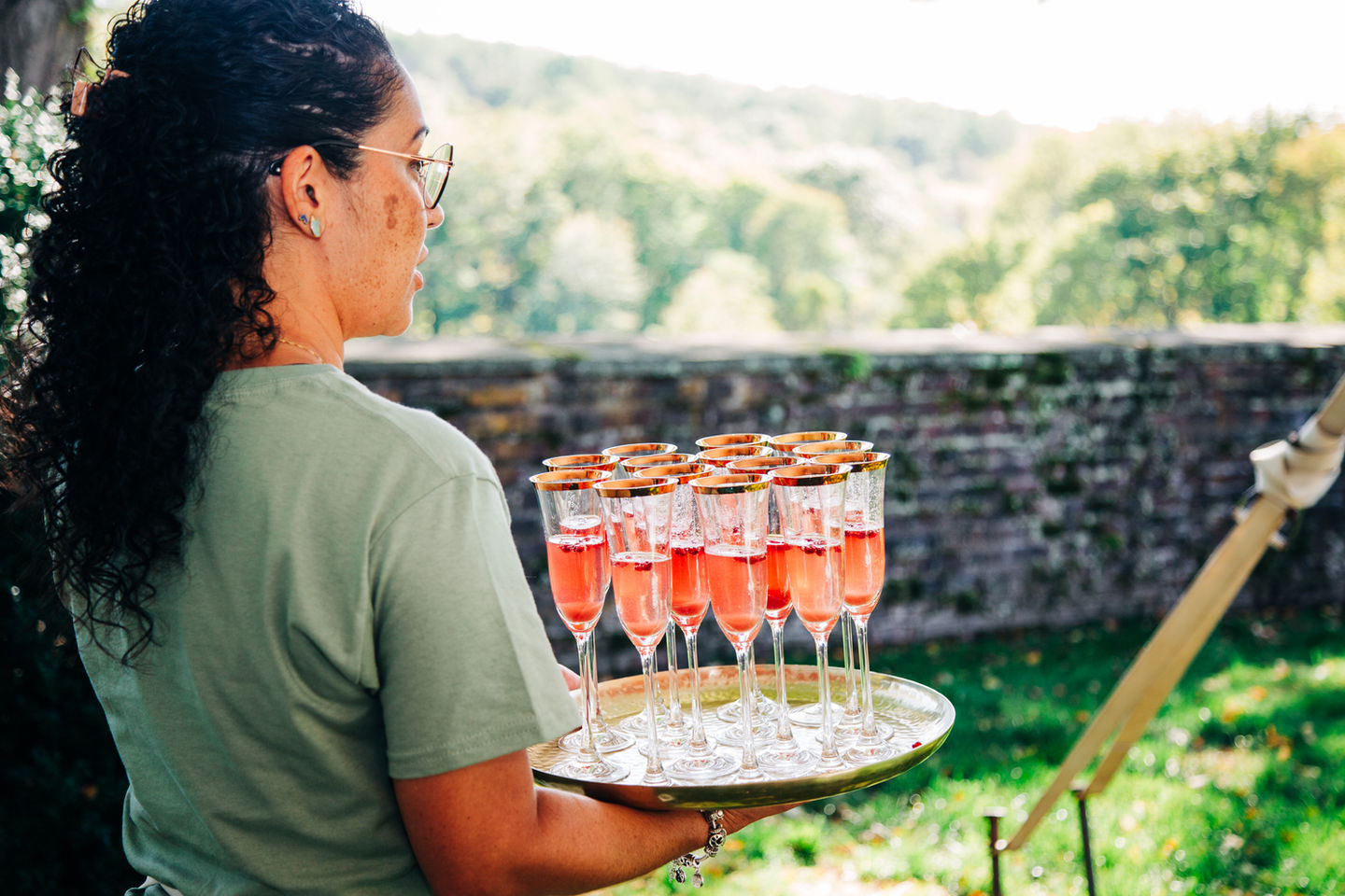 Server carrying a tray of champagne cocktails at an outdoor wedding catered by Tia’s Food of Love.