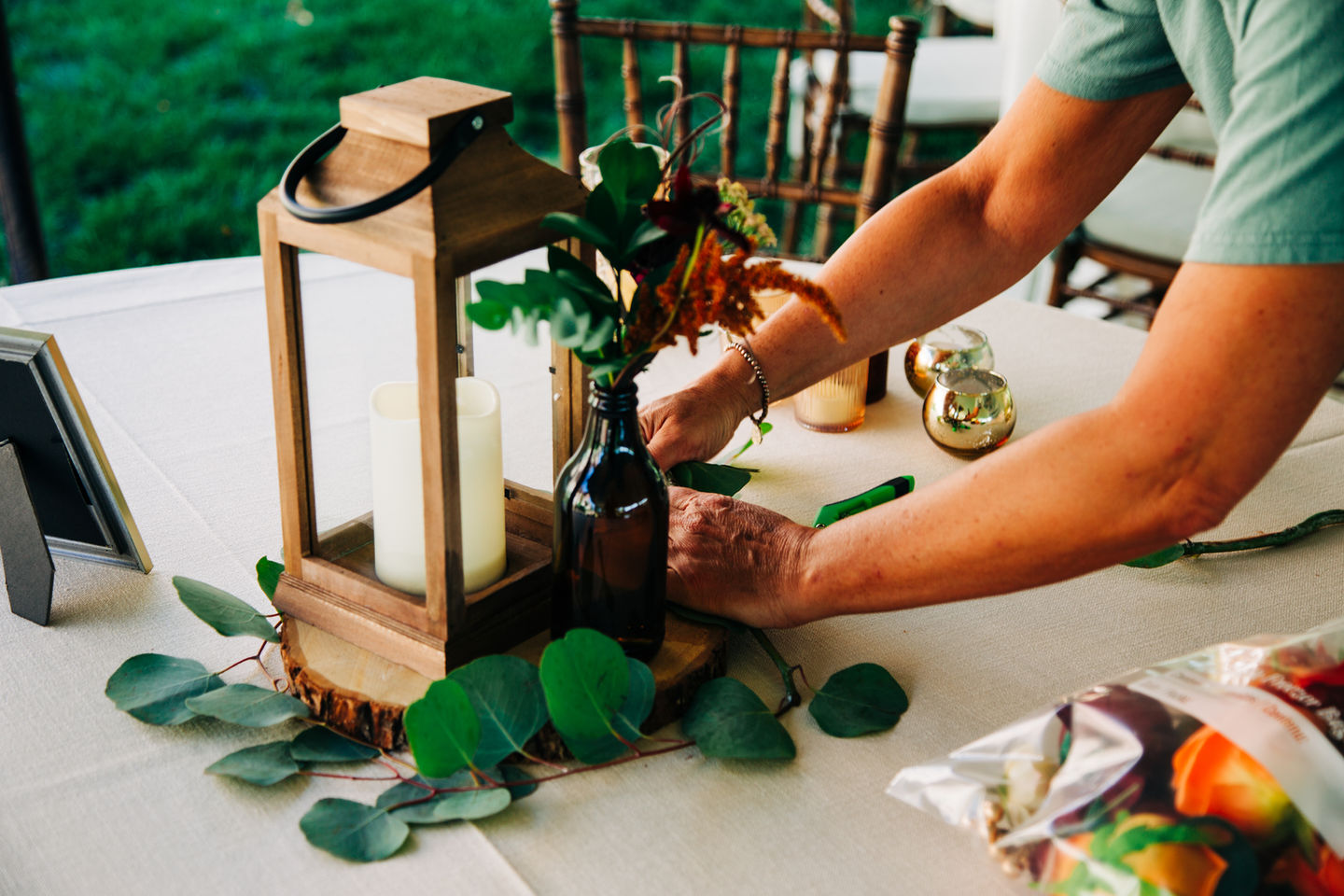 Wooden lantern centerpiece with eucalyptus greenery and floral accents on a wedding reception table, styled by Tia’s Food of Love.
