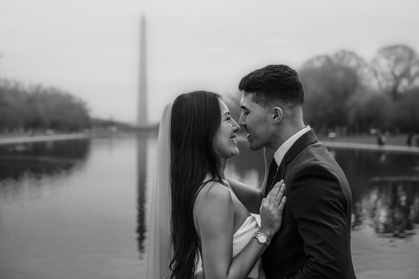 Bride and groom sharing a tender moment near the Reflecting Pool with the Washington Monument behind them.