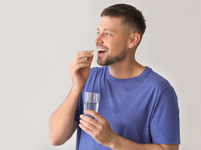 A man taking an oral supplement while holding a glass of water in the other hand